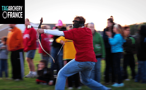 Photo du club Tag Archery  une personne tenant un arc bandé avec un groupe de gens en fond. 